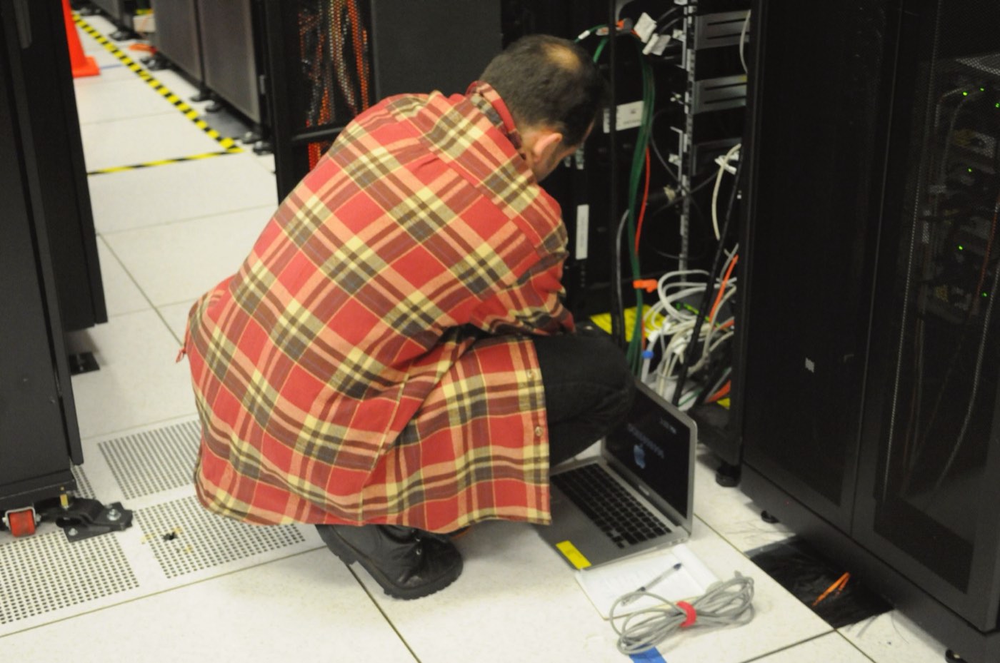 An engineer works on a laptop beside open server racks